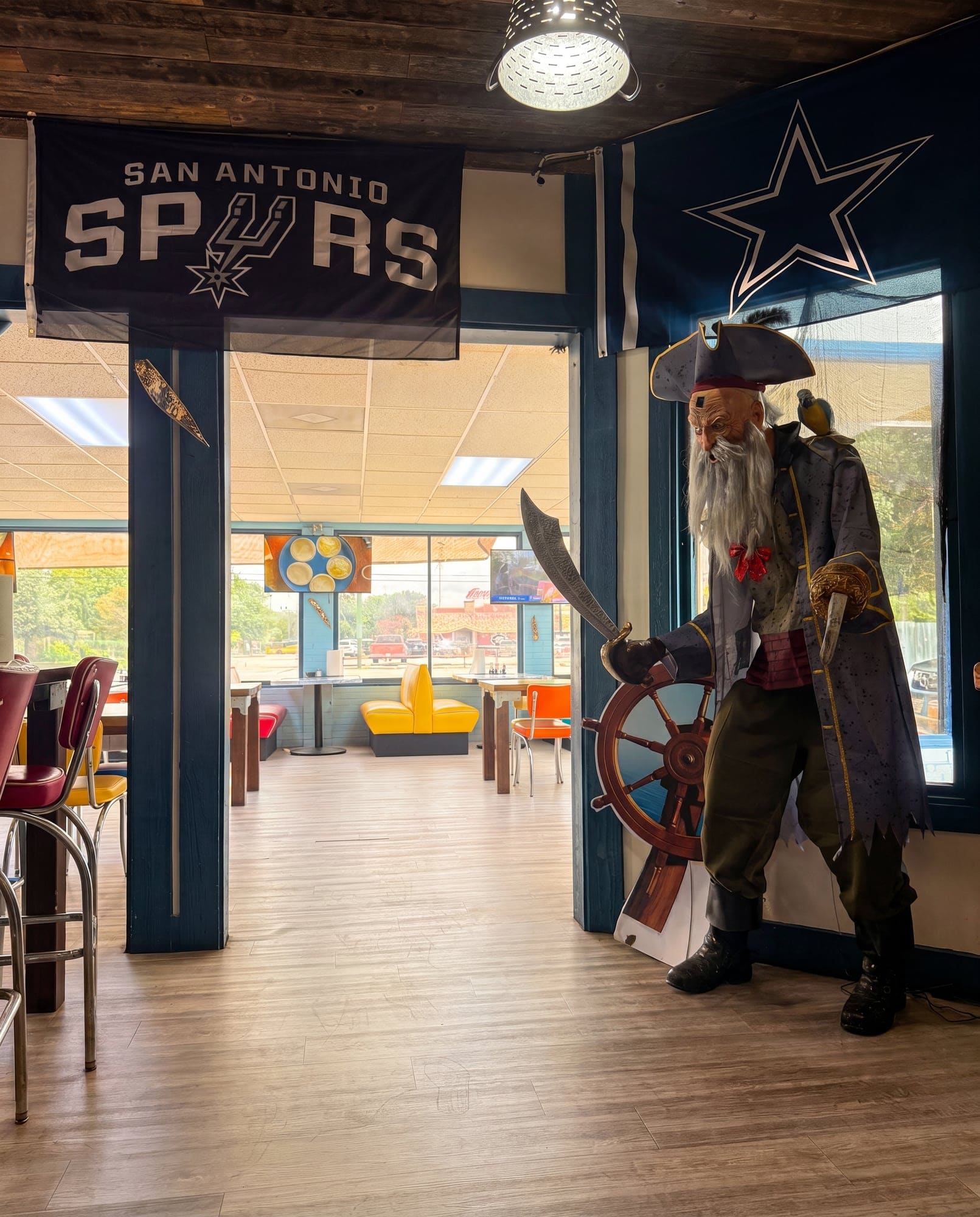 The life-size pirate at the ship's wheel inside El Pirata — Spurs banner and Cowboys star